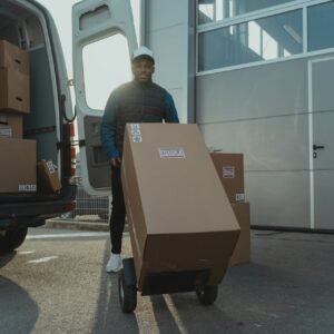 Delivery man with trolley unloading boxes from a van outside a warehouse.